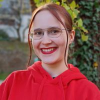 Lena Lang, lächelnd mit schulterlangem Haar und Brille