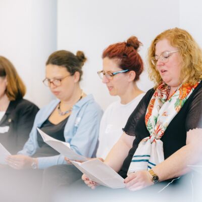 Fünf Frauen sitzen in einer Reihe und singen aus dem Liedheft.