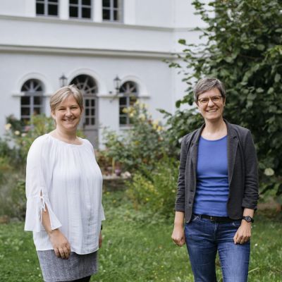 Zwei Frauen stehen im Grünen vor einem Tagungshaus.