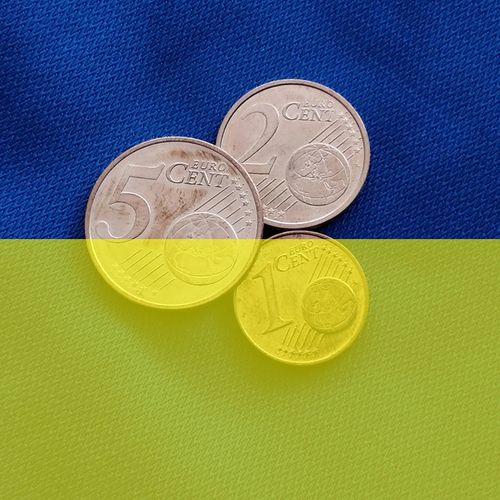Auf einem dunkelblauen Stoff liegen drei kupferne Centmünzen. Der untere Bilddteil ist gelb eingefärbt, sodass das Gesamtbild die Farben der ukrainischen Flagge zeigt.