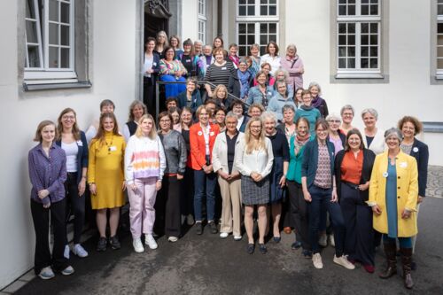 Junge und ältere Frauen stehen vor und auf einer Treppe.